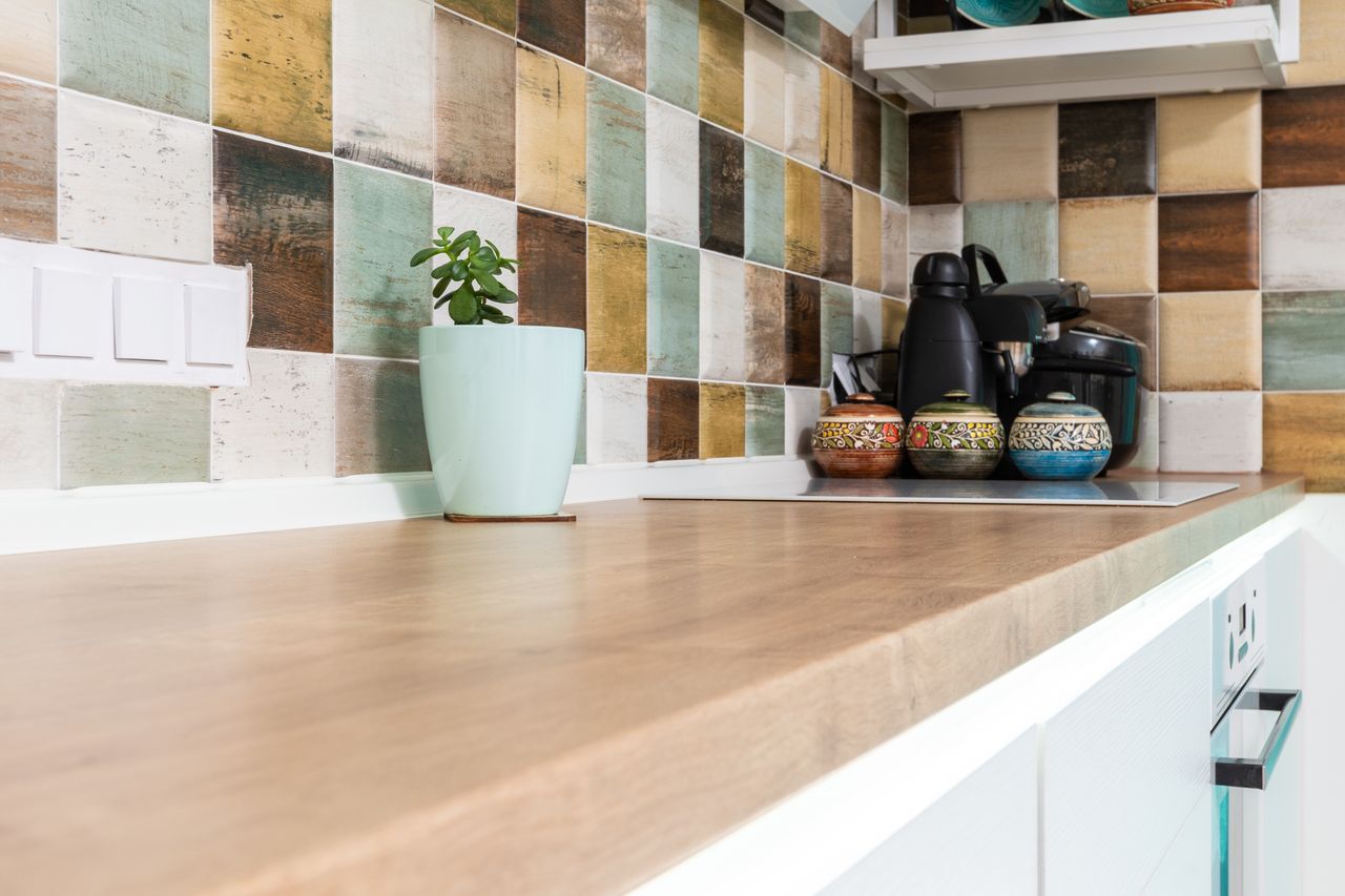 contact-img Interior of light kitchen furnished with wooden counter with multicolored tiled backsplash and various dishware